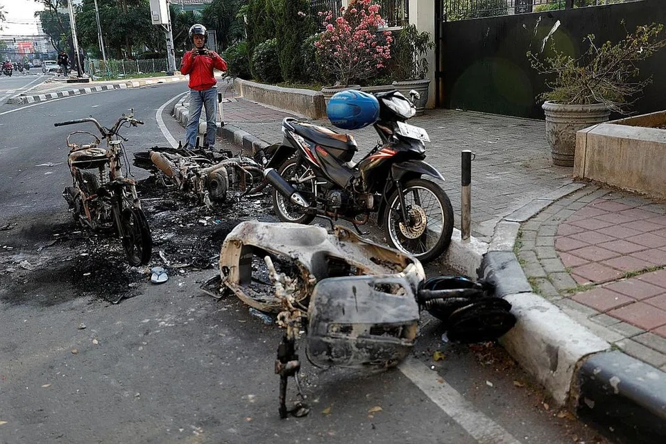 TINGGAL SISA: Lelaki ini mengambil gambar motosikal-motosikal yang dibakar semasa rusuhan di Jakarta kelmarin. - Foto REUTERS