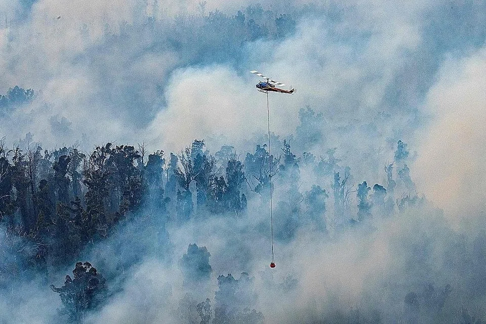 LANGKAH MELAWAN API DARI UDARA: Sebuah helikopter menyembur air di kawasan kebakaran di wilayah Gippsland di timur Victoria. Para pelancong dan anggota bomba diarah keluar dari kawasan kebakaran besar di tenggara Australia semalam. - Foto AFP