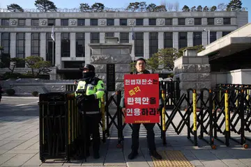 Seorang lelaki berdiri sambil memegang papan tanda yang bertulis, “Mahkamah Perlembagaan harus segera menerima pemecatan Presiden Yoon Suk Yeol” di hadapan Mahkamah Perlembagaan di Seoul pada 16 Disember. 