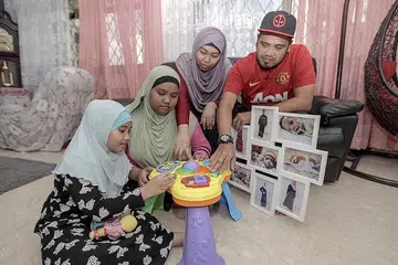DALAM INGATAN: Encik Mohd Jazlan Hamzah (kanan) dan isteri, Cik Siti Zubaidah Mohd Daud (dua dari kanan) reda dengan pemergian anak bongsu mereka Armel Nadia, yang mengalami Sindrom Down dan meninggal dunia Sabtu lalu kerana kesulitan penyakit paru-paru kronik. Dua anak mereka (dari kiri) Qisya Asmara dan Anggun Farisya turut mengingati keceriaan adik mereka. - Foto BH oleh IQBAL FAIZAL