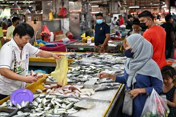 Seorang pegerai sedang menjual ikannya kepada pelanggan di pasar basah Pandan di Johor Bahru.