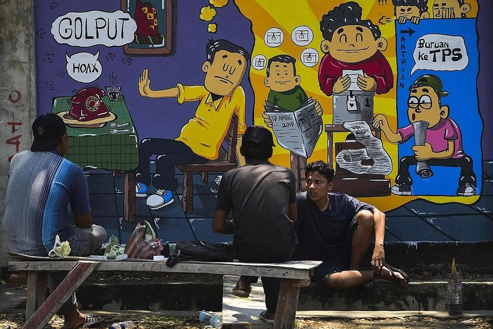 GESA RAKYAT MENGUNDI: Penduduk bersembang di depan mural kempen pilihan raya Indonesia, yang menyeru rakyat supaya keluar mengundi pada 17 April, di Banda Aceh, ibu negeri wilayah Aceh. - Foto AFA 