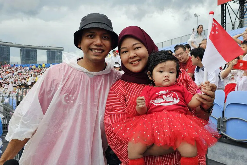 Cik Sudriyanti Samsudin (kanan), suami Encik Mohamad Sidiq Johari (kiri), kedua-duanya 36 tahun, dan anak perempuan mereka berusia 10 bulan, Qaizara Mohamad Sidiq (didukung ibunya), mengharungi hujan untuk merasakan semangat kesingapuraan 9 Ogos.