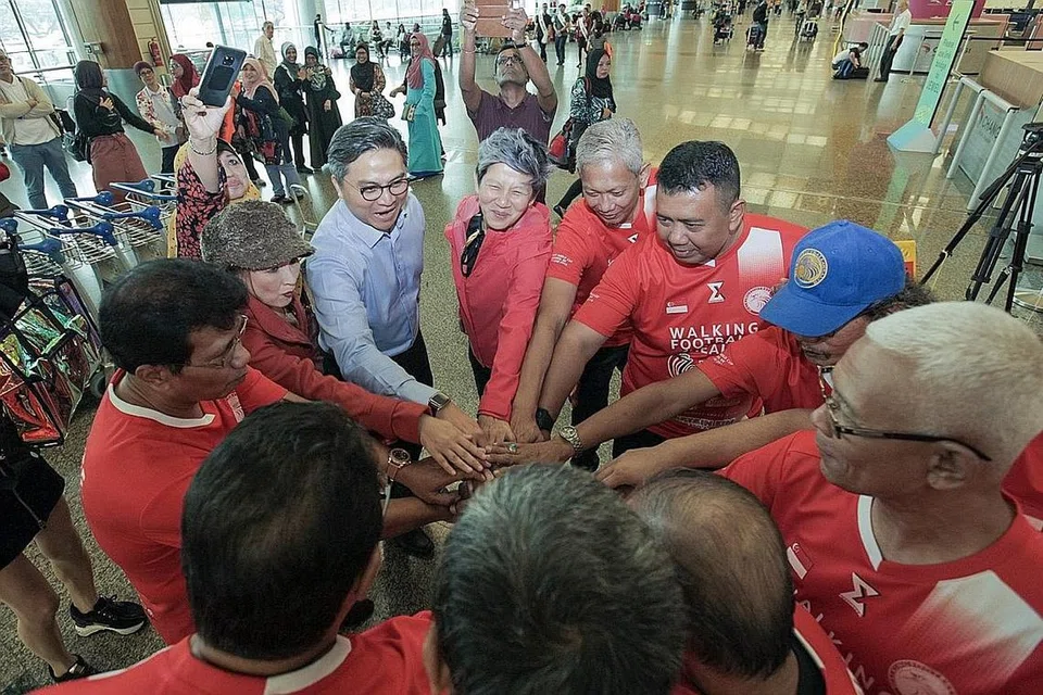 SORAKAN GEMURUH: Encik Saktiandi Supaat (berbaju biru) memberi sokongan kepada pasukan Singapura yang akan mewakili negara di Pertandingan Sepak Bola Berjalan di England. Turut hadir ialah Dr Dee Dee (bertopi) dan Cik Elim Chew (berjaket merah jambu), salah seorang penaja acara. - Foto BH oleh IQBAL FAIZAL