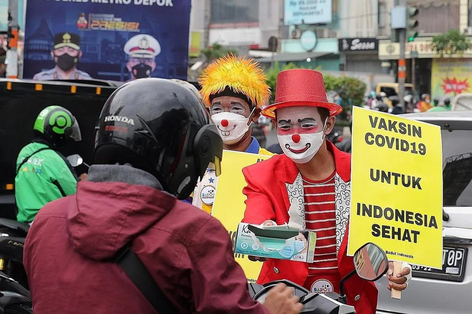 BUKAN LAWAK: Anggota kumpulan badut 'Aku Badut Indonesia (ABI)' memakai topeng muka pelindung memegang poster kempen menggalak penduduk negara itu mendapatkan vaksin Covid-19 di Depok, Jawa Barat Jumaat lalu. Indonesia mencatat lebih 3,000,000 kes Covid-19 dengan lebih 82,000 kematian sejak awal pandemik itu. - Foto EPA-EFE