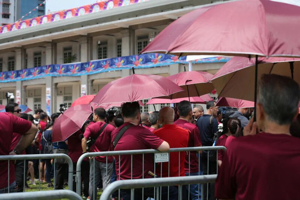 PANAS TERIK: Penyokong Encik Tharman boleh dilihat berpakaian warna merah manggis dan menggunakan payung yang sama warna.