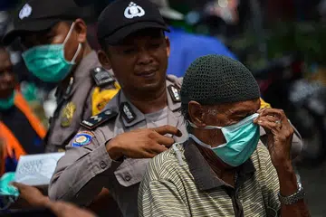 HUJAN BAWA KELEGAAN: Seorang pegawai polis membantu seorang penunggang motosikal memakai pelitup muka di Banda Aceh, Sumatera, kelmarin. Terdapat 3,150 titik panas di seluruh Indonesia Isnin lalu. Tetapi Selasa lalu, bilangan itu menjunam kepada 1,982 titik sebelum turun ke 1,744 titik kelmarin - Foto AFP