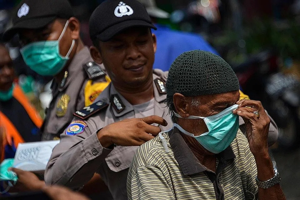 HUJAN BAWA KELEGAAN: Seorang pegawai polis membantu seorang penunggang motosikal memakai pelitup muka di Banda Aceh, Sumatera, kelmarin. Terdapat 3,150 titik panas di seluruh Indonesia Isnin lalu. Tetapi Selasa lalu, bilangan itu menjunam kepada 1,982 titik sebelum turun ke 1,744 titik kelmarin - Foto AFP