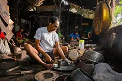 Tiga petukang sedang bertugas di stesen masing-masing dengan setiap seorang menumpukan perhatian pada peringkat berbeza dalam proses menghasilkan gamelan.