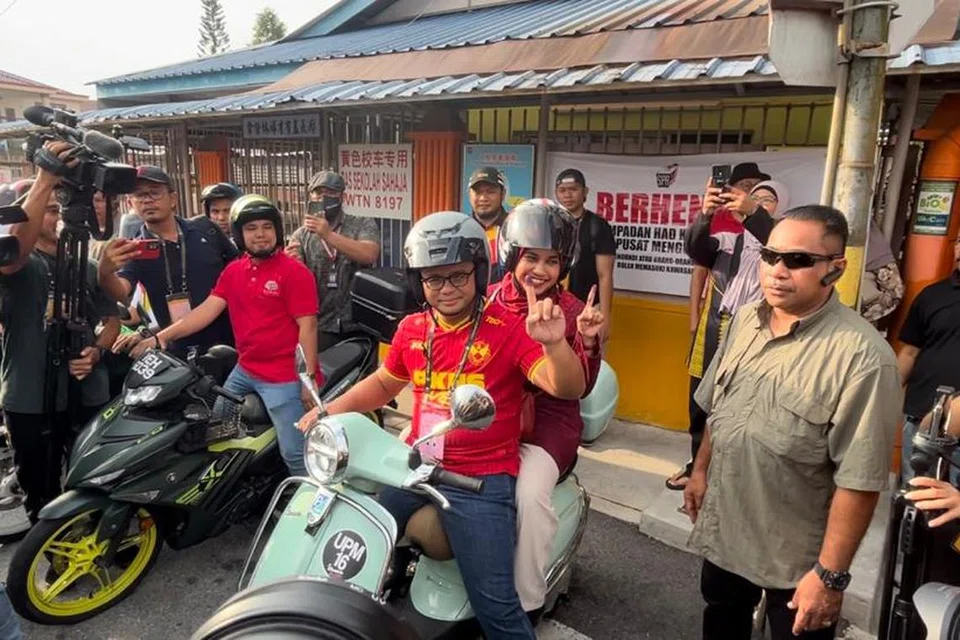CURI TUMPUAN: Calon Pakatan Harapan bagi kerusi Dewan Undangan Negeri (DUN) Sungai Tua, Datuk Seri Amirudin Shari (mengangkat tangan), bersama isteri, Datin Seri Masdiana Muhamad, yang menaiki skuter ke pusat pengundian Sekolah Jenis Kebangsaan Cina Selayang Baru, Gombak, Selangor mencuri tumpuan ramai.