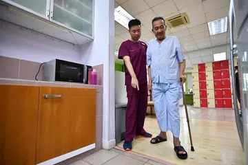MODEL PENJAGAAN BARU: Encik Max Lim, seorang jurupulih pekerjaan kanan, membantu membimbing seorang pesakit melakukan kegiatan harian di Pusat Pemulihan Hospital Alexandra.
