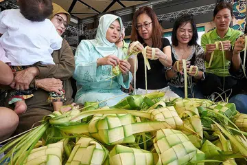 ANYAM KETUPAT: Cik Rahayu (dua dari kiri) menganyam ketupat bersama pemimpin akar umbi Bukit Batok East, Cik Cynthia Lim (paling kanan) dan Cik Teo Ai Leng (tiga dari kanan) serta relawan kawasan Bukit Batok East, Cik Josephine Wong (dua dari kanan) di Wisma Geylang Serai dalam acara 'Ketupat-thon' semalam. Cik Rahayu ditemani ibunya, Cik Kasmawati Manijan (paling kiri) yang sedang mendukung anak Cik Rahayu, Muhamad Ayden Muhamad Imaduddien. - Foto BH oleh ROSLEE ABDUL RAZAK