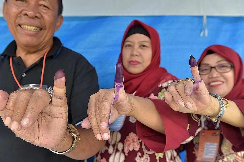 SUDAH UNDI: Penduduk setempat menunjukkan jari mereka yang telah dicelup dakwat selepas membuang undi semasa pilihan raya daerah di Tangerang, Banten, semalam. - Foto AFP 
