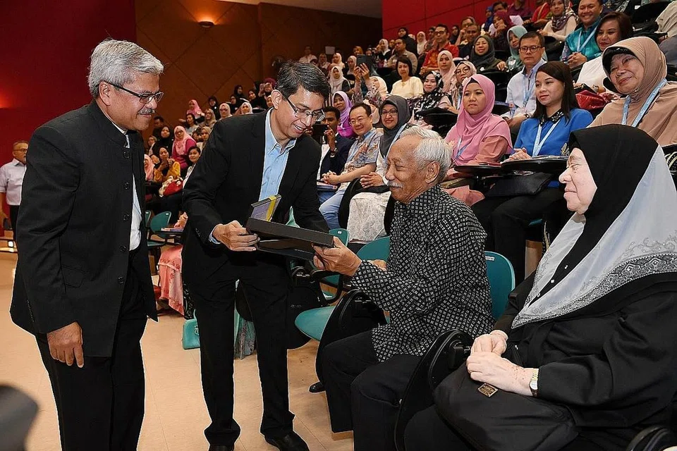 BAHAN PENERBITAN MENARIK: Dr Muhammad Faishal Ibrahim bersama Pengarah Pusat Bahasa Melayu Singapura Encik Mohamed Noh Daipi (kiri) sedang memberikan cenderahati kepada tokoh batik tersohor, Encik Sarkasi Said (duduk) semasa pelancaran penerbitan video Bicara Budiman di Seminar Bahasa Melayu 2019. - Foto BH oleh KHALID BABA