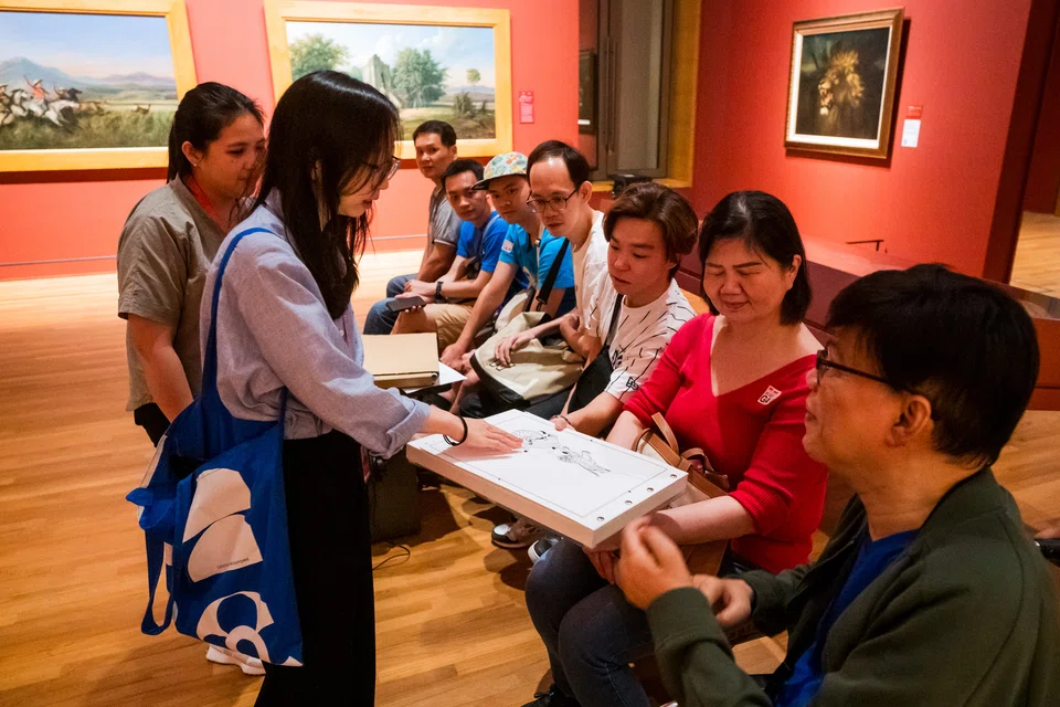 Seorang kakitangan Jabatan Komuniti dan Akses di Galeri Nasional Singapura menjadi jurupandu bagi sekumpulan peserta dengan pelbagai jenis ketidakupayaan, menggunakan buku dengan penekanan pada unsur sentuhan, daripada koleksi, ‘Hands on Learning and Development’ (Hold).