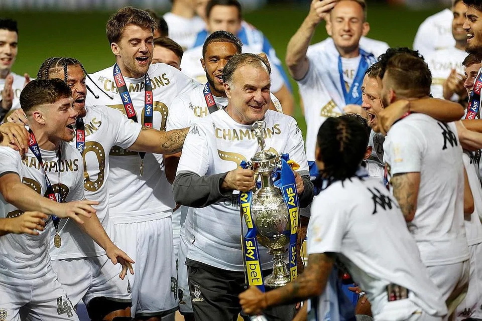 KEMUNCULAN YANG DINANTI: Pengurus Leeds United Marcelo Bielsa (memegang trofi) semasa meraikan kemenangan pasukannya dalam Liga Championship Julai lalu dan sekali gus dinaikkan ke EPL. Bielsa akur berdepan ujian sukar di Anfield awal pagi esok iaitu perlawanan Liga Perdana pertama kelab itu dalam 16 tahun. - Foto REUTERS