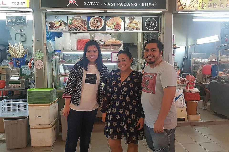 MAHU MEMBANTU: Cik Shah Hida (tengah) dan suaminya Encik Zulkifli di depan gerai mereka di Pusat Penjaja Tiong Bahru bersama Cik Cheryl Cadeline Lee yang menyarankan idea hari istimewa 'Bad Day Meal'. - Foto ihsan SHAH HIDA ANUAR