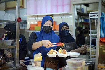 PRIHATIN PADA PELANGGAN: Cik Ashiqin Tuan Anuar (depan, kiri), 30 tahun dan ibunya Cik Noor Hayathi Haji Mahmood (depan, kanan), 53 tahun mengendalikan gerai Best Food Forever Malay Cuisine di Kelab Masyarakat Pasir Ris East. - Foto BH oleh HARITH MUSTAFFA