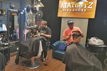 GUNTING AMAL: Encik Effendy Ali (kanan, berbaju warna jingga) menggunting rambut pelanggan di kedai gunting lelaki Atatcutz Singapore di Simpang Bedok. Beliau membuka kedai itu November lalu dan sejak itu telah menyertai beberapa acara gunting rambut amal buat golongan berpendapatan rendah. - Foto ATATCUTZ SINGAPORE