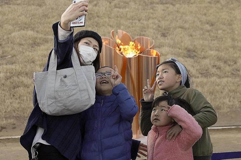 MUNGKIN DITUNDA: Penduduk berswafoto berlatarbelakangkan kawah api Olimpik di Ishinomaki, wilayah Miyagi di Jepun pada Jumaat lalu. IOC telah membuat pusingan-U separa kelmarin selepas begitu lama menekankan, bersama Tokyo, bahawa Sukan Tokyo 2010 akan diteruskan mengikut jadual. - Foto EPA-EFE