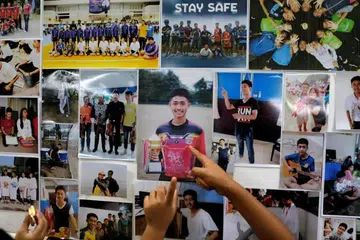 PENANTIAN SUKAR: Gambar-gambar kanak-kanak lelaki yang terperangkap dalam gua Tham Luang ditampal di papan tanda sementara yang dipasangkan berdekatan gua Tham Luang. 