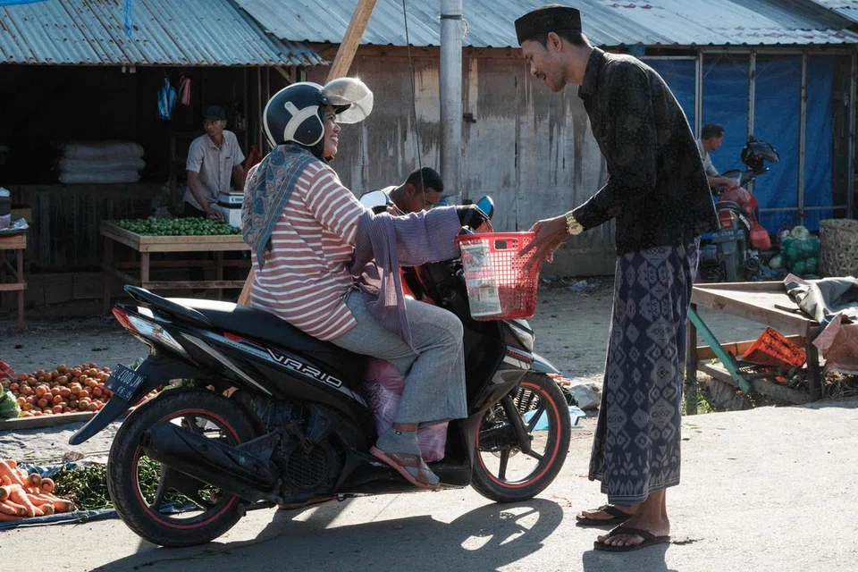 Seorang wanita menaiki skuter memberikan sumbangan wang kepada seorang lelaki yang mengutip derma di Pasar Tradisional Al Mahirah, Banda Aceh, pada 27 Disember 2024.