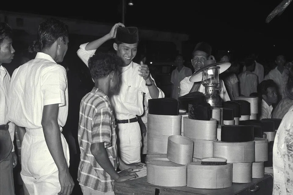 Seorang pemuda mencuba songkok di sebuah gerai jualan di Geylang Serai menjelang Hari Raya pada 16 Mac 1961.  