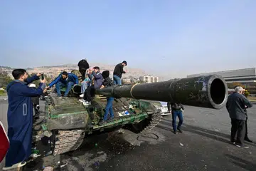 Orang ramai bergambar di atas sebuah kereta kebal yang ditinggalkan di Dataran Umayyad, Damsyik pada 10 Disember. Pemimpin pemberontak Syria pada 9 Disember memulakan perbincangan mengenai proses penyerahan kuasa, sehari selepas gabungan pembangkangnya secara dramatik menyingkirkan Presiden Bashar al-Assad.