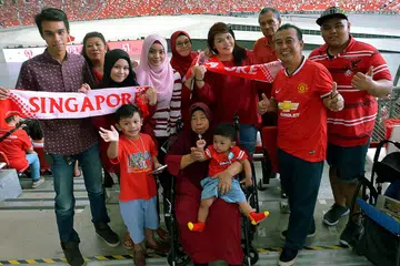 KELUARGA BESAR DI NDP: Cik Rozila (tudung merah, berkaca mata) dan keluarga besarnya yang merangkumi empat generasi merupakan antara sekitar 55,000 penonton yang mencipta sejarah menyaksikan NDP di Stadium Negara buat kali pertama setelah ia dibina semula.