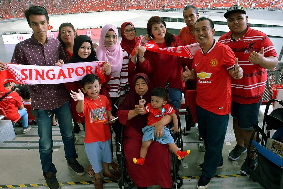 KELUARGA BESAR DI NDP: Cik Rozila (tudung merah, berkaca mata) dan keluarga besarnya yang merangkumi empat generasi merupakan antara sekitar 55,000 penonton yang mencipta sejarah menyaksikan NDP di Stadium Negara buat kali pertama setelah ia dibina semula.