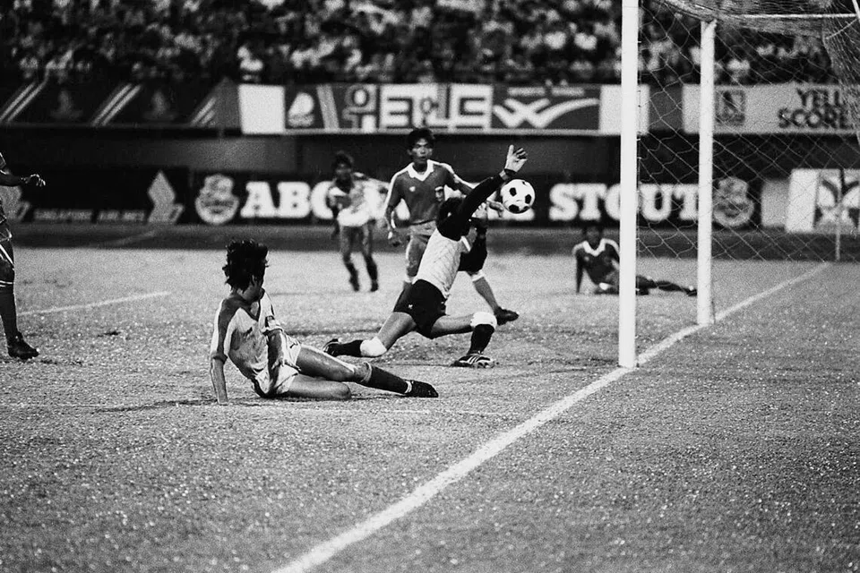 Pemain tengah Singapura, Malek Awab dari Singapura (kiri), melihat rembatannya melepasi penjaga gol Indonesia, Sobur, tetapi malangnya ia tidak menghasilkan gol.  Ia merupakan pertembungan antara Singapura dengan Indonesia di perlawanan pertama Piala Merlion di Stadium Nasional pada 3 Disember 1983, di mana pasukan negara menang 5-0.