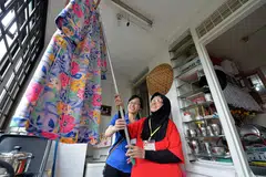 KEHIDUPAN DIBANTU: Seorang warga emas, Cik Hindon Abdullah (berbaju merah) dibantu seorang sukarelawan untuk menyidai baju di flat 'L' beliau di Toa Payoh Lorong 7. Beliau diantara mereka yang dibantu Pusat Kegiatan Warga Emas Care Corner. - Foto fail