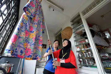 KEHIDUPAN DIBANTU: Seorang warga emas, Cik Hindon Abdullah (berbaju merah) dibantu seorang sukarelawan untuk menyidai baju di flat 'L' beliau di Toa Payoh Lorong 7. Beliau diantara mereka yang dibantu Pusat Kegiatan Warga Emas Care Corner. - Foto fail