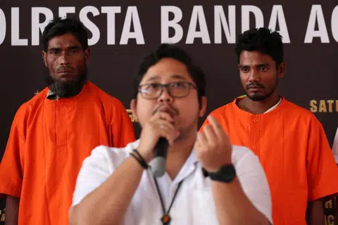 DALANG DIKENAL PASTI: Dua suspek, warga Bangladesh dan Rohingya berdiri di belakang sedang pegawai polis Aceh, Encik Fadillah Aditiya Pratama, bercakap dalam sidang akhbar berhubung kes penyeludupan pelarian Rohingya di pejabat polis di Banda Aceh, Indonesia.