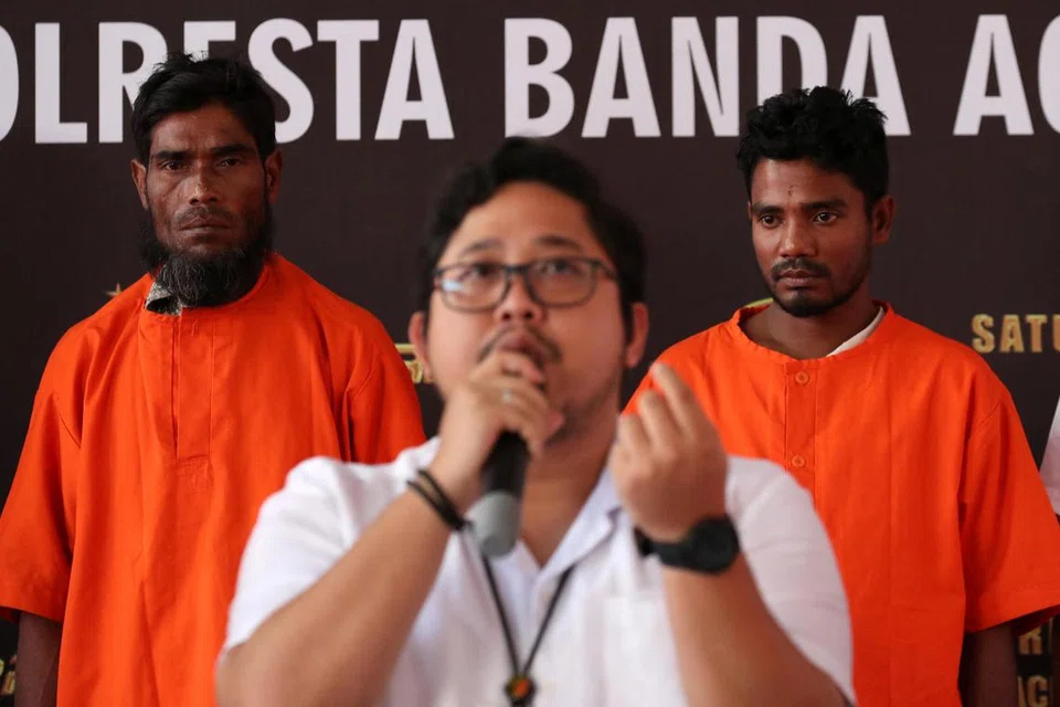 DALANG DIKENAL PASTI: Dua suspek, warga Bangladesh dan Rohingya berdiri di belakang sedang pegawai polis Aceh, Encik Fadillah Aditiya Pratama, bercakap dalam sidang akhbar berhubung kes penyeludupan pelarian Rohingya di pejabat polis di Banda Aceh, Indonesia.