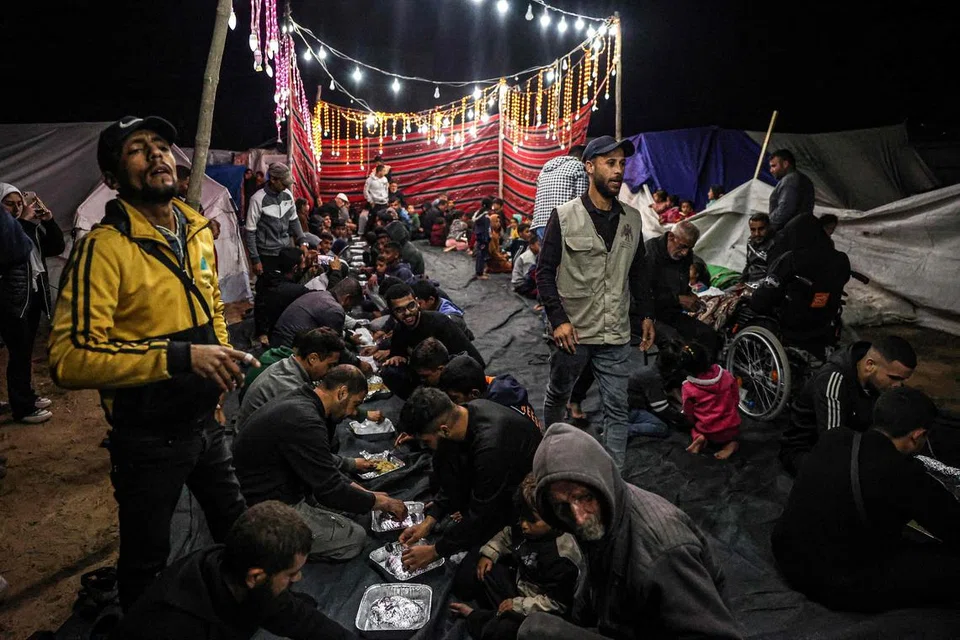 Rakyat Palestin berkongsi hidangan berbuka puasa pada hari pertama bulan Ramadan, di sebuah kem untuk orang yang kehilangan tempat tinggal di Rafah di selatan Jaluran Gaza pada 11 Mac, di tengah-tengah pertempuran berterusan antara Israel dengan Hamas.