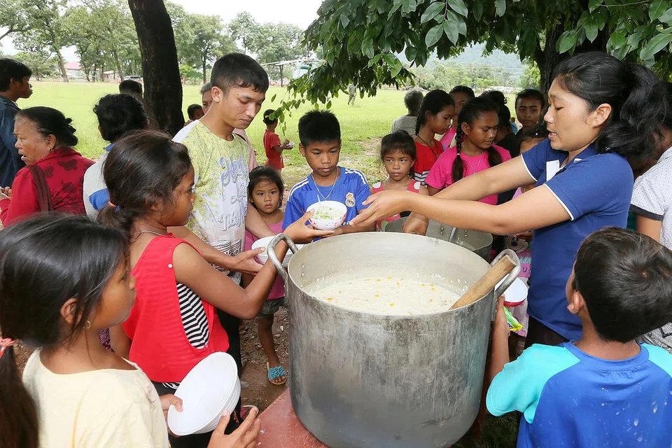 HIDANG BUBUR: Relawan menghidangkan bubur kepada penduduk yang terjejas di pusat pemindahan Sanamxay.