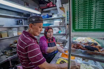 KEMBALI BERNIAGA: Encik Zainon Ahmad dan isterinya, Cik Zaiton Shaik Vali Ahmad, berasa gembira kerana akhirnya boleh kembali berniaga selepas gerai mereka di Pasar dan Pusat Makanan Tekka dibuka semula pada Ahad sejak ia ditutup tiga bulan lalu.