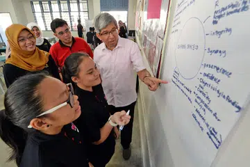 FAHAMI KEPERLUAN PELAJAR: (Dari kiri) Ketua Pegawai Eksekutif (CEO) Mendaki, Cik Rahayu Buang; Encik Adri; dan Dr Yaacob, melihat catatan pelajar Skim Tuisyen Mendaki (MTS) mengenai keperluan mereka di sesi tuisyen pertama semalam. - Foto ZAINAL YAHYA