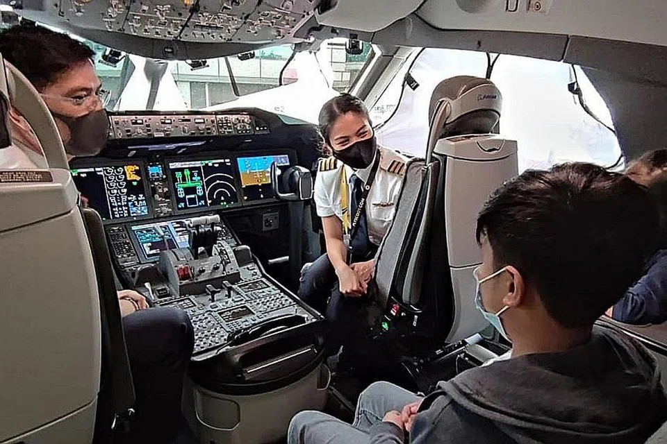 MENEROKA KOKPIT: Cik Farhain (tengah) mendekati anak-anak semasa lawatan mereka ke dalam kokpit kapal terbang 787 Dreamliner Scoot. - Foto SCOOT