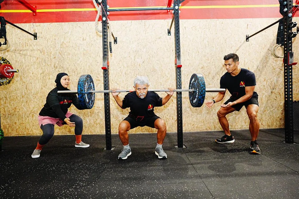 Encik Jumahat (tengah) ankat biasa (deadlift) seberat 60 kilogram dan anak-anaknya menyokong berat dari tepi.