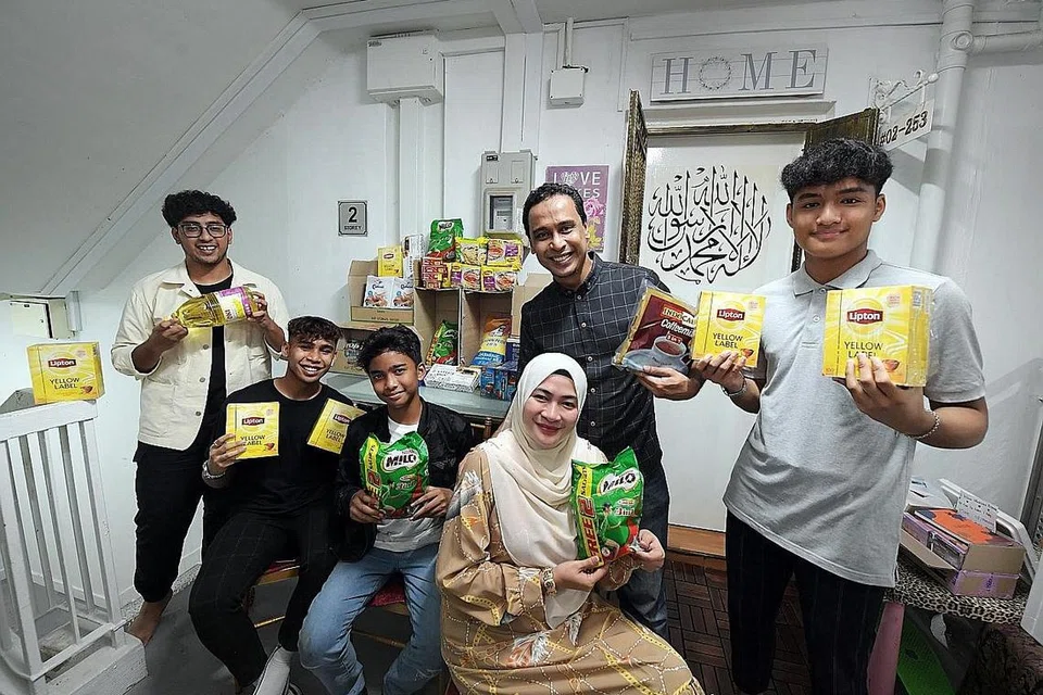 'KEDAI RUNCIT' PERCUMA: Encik Fariq (tengah, di belakang) bersama isteri, Cik Norhasyimah dan anak-anak mereka (dari kiri) Muhammad Nabil Putra, Hilman Aqil Zulikram Putra, Irfan Danial Putra dan Hamzah Lutfil Putra, di ruang infak di depan flat mereka di Tampines. - Foto BH oleh ALPHONSUS CHERN 
