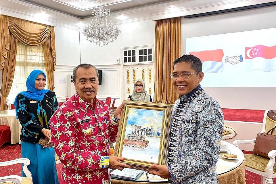 IKATAN DIPERKUKUH: Dr Maliki menyampaikan hadiah lukisan hasil karya artis Ng Siang Hoi dari Very Special Arts Singapore Ltd (VSA) - sebuah badan amal yang memberikan individu berkeperluan khas akses kepada seni - kepada Gabenor Riau, Encik Syamsuar, semasa pertemuan mereka di Pekanbaru baru-baru ini. - Foto DR MALIKI OSMAN/FACEBOOK