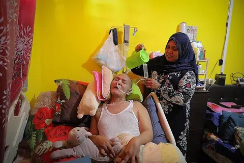 PENJAGA SEPENUH MASA: Cik Norlindah Roslan, 35 tahun, berhenti kerja dan menjadi penjaga sepenuh masa suaminya, Encik Omar Anoor, 52 tahun, yang terlantar di katil sejak dua tahun lalu. - Foto BH oleh ONG WEE JIN