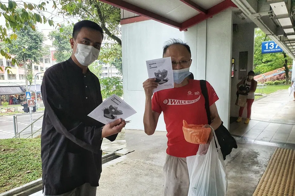 Pengurus Masjid Darul Makmur, Ustaz Ruhaizan Abdullah (kiri), memberi risalah kepada penduduk bukan Islam yang menerima bubur Ramadan di kolong Blok 137 Yishun Ring Road pada 2023 anjuran bersama MAEC Chong Pang.