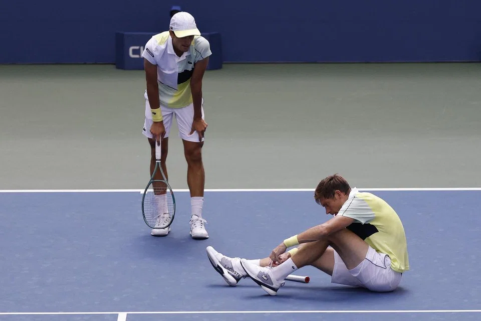 RASA PENING: Nicolas Mahut dari Perancis duduk di atas lantai gelanggang selepas mengalami pening akibat cuaca terlalu panas sambil rakan gandingannya,  Pierre-Hugues Herbert juga dari Perancis memandangnya. 