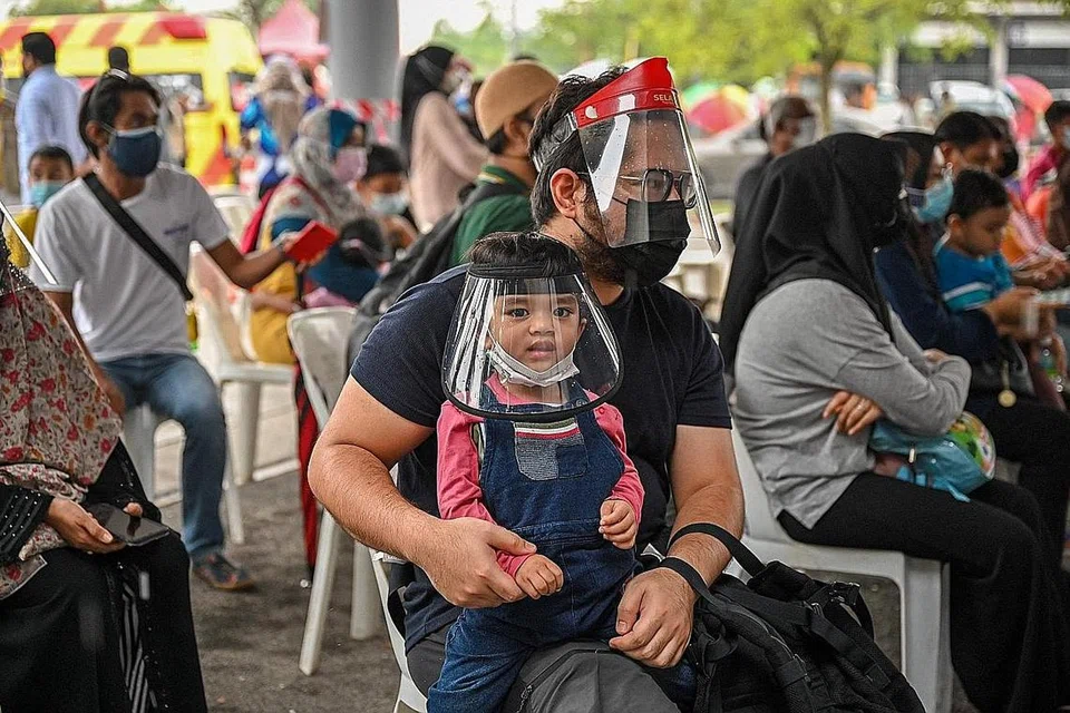 JALANI VAKSINASI: Seorang bapa bersama anak lelaki yang dipangkunya sedang menunggu ujian pemeriksaan percuma bagi mengesan Covid-19 di sebuah pusat pemeriksaan kesihatan di Shah Alam, Selangor, pada 27 Mei lalu. - Foto AFP