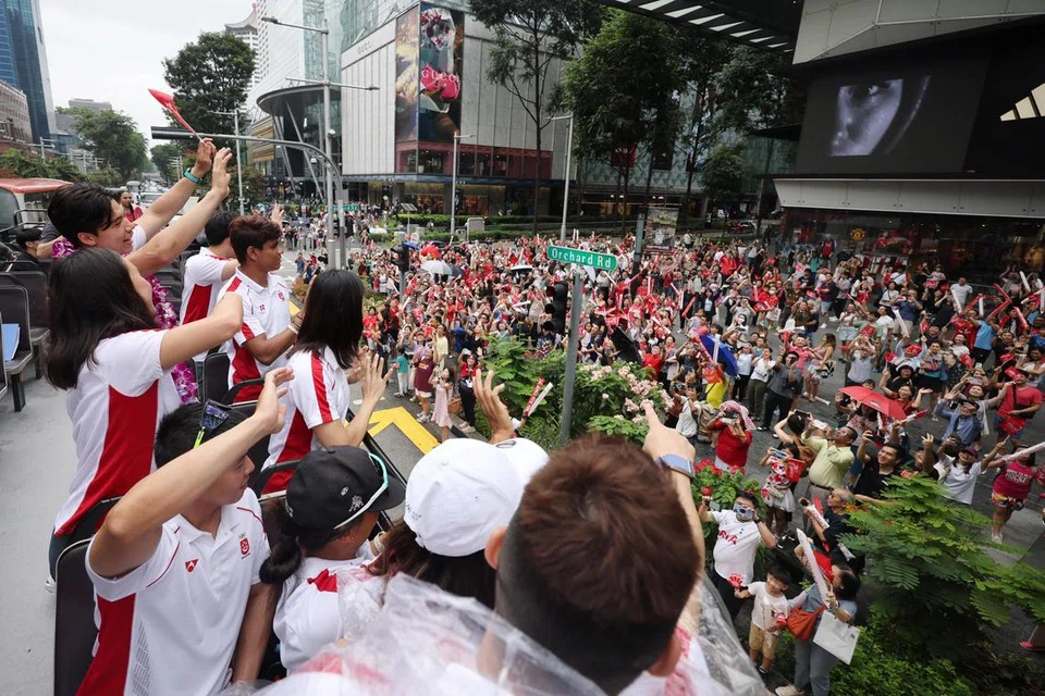 Atlet Olimpik Singapura melambai kepada penyokong semasa perarakan melalui Orchard Road pada 14 Ogos, yang juga merupakan titik sorakan ketiga dalam perjalanan bas mereka. 