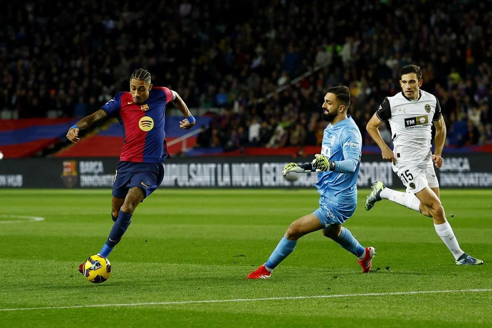 Penyerang Barcelona, Raphinha (paling kiri), melepasi penjaga gawang Valencia, Giorgi Mamardashvili, untuk gol ketiga Barcelona.  