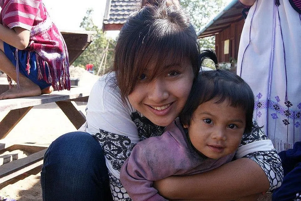 TABUR BAKTI: Cik Nadia semasa menjadi mahasiswi Universiti Pengurusan Singapura (SMU) merangkul seorang kanak-kanak ketika menjadi relawan di kampung terpencil di utara Thailand. - Foto fail 